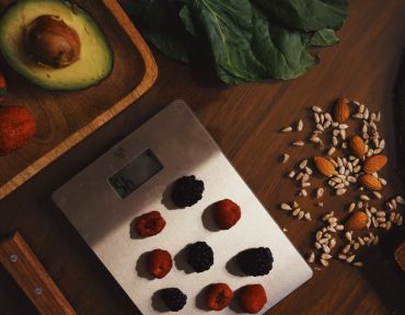 Top view of composed raw almond with seeds and avocado on table with berries on scales for cooking healthy dish